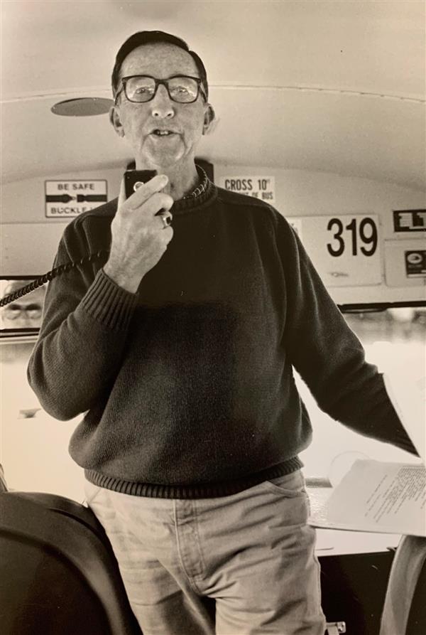 Jack Gaffney standing at the front of a bus holding the microphone to speak